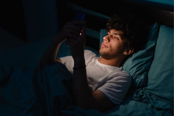 homme allongé dans son lit devant son téléphone portable